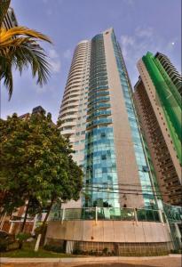 un edificio alto con una palmera delante de él en Quarto em condomínio beira-mar en Recife