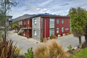 an apartment building with a red facade with mountains in the background at Lakeshore Studio at the Marina in Queenstown