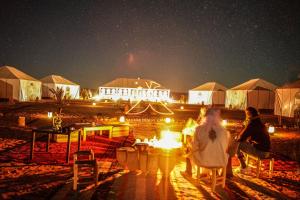a group of people sitting around a fire at night at Sahara Desert Camping - Luxury Desert Camp Merzouga in Erfoud