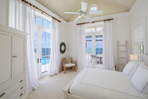 a white bedroom with a bed and large windows at Ambergris Cay Private Island All Inclusive in Big Ambergris Cay