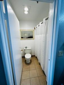 a bathroom with a toilet and white shower curtain at Casa Blanca Express & Suites Cypress Buena Park - Anaheim Area in Cypress