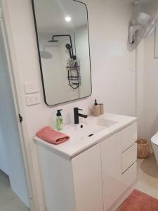 a white bathroom with a sink and a mirror at Adorable 2 bedroom unit, set in lush gardens in McMinns Lagoon