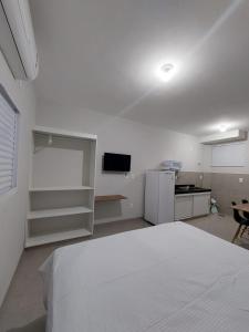 a white room with a white bed and a kitchen at FLAT SABIÁ in Uberlândia