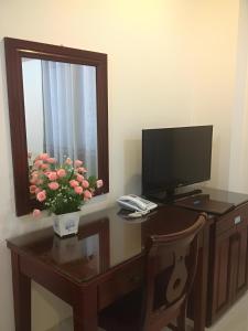 a desk with a computer monitor and a vase of flowers on it at KIM BĂNG HOTEL BÌNH DƯƠNG in Thu Dau Mot +8 photos