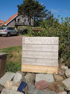 Un cartello su alcune rocce con una casa sullo sfondo di De Oostkamer; Eiland appartement naast natuurgebied Boschplaat a Oosterend