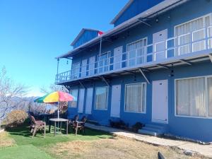 a blue building with a table and an umbrella at IN APPLE ESTATE KANATAL - Himalayan View Resort with Courteous Staff in Kanatal