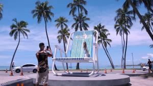 a man taking a picture of a woman sitting in a blue chair at Verano Pajuçara by Tropicalis in Maceió