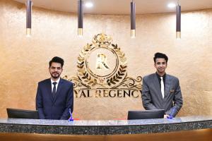dos hombres de traje parados en un mostrador frente a una señal en Royal Regency Hotel en Islamabad
