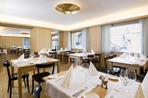 un restaurante con mesas y sillas blancas y ventanas en Hotel Alpina, en Vals