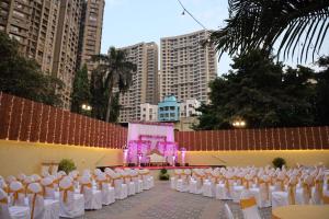 a banquet hall with white chairs and a stage at Maple Inn in Thane