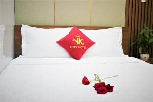 Una cama con una almohada roja y dos rosas. en Khách Sạn K’My, en Ấp Phú Thọ