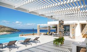 eine Terrasse mit Stühlen, einem Pool und dem Meer in der Unterkunft Haven Villa in Ierápetra