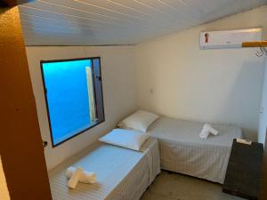 2 Betten in einem kleinen Zimmer mit Fenster in der Unterkunft Casa da Lua no centro da Vila de Caraíva ao lado da Igreja de Caraíva in Caraíva