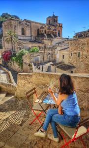 kobieta siedząca przy stole w krześle patrząca na zamek w obiekcie Lilibeth Houses - Charming & Lovely views w mieście Scicli