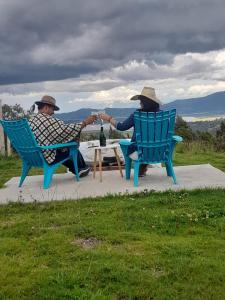 dois homens sentados em cadeiras de mãos dadas numa mesa em Cabañas camino al cielo em Fúquene