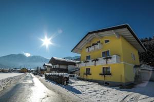 un bâtiment jaune dans une rue enneigée avec le soleil derrière dans l'établissement Appartements Haidl, à Sankt Johann im Pongau