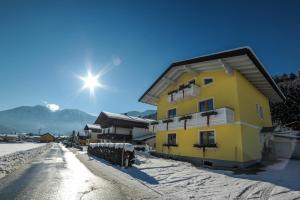 ein gelbes Gebäude auf einer verschneiten Straße mit der Sonne dahinter in der Unterkunft Appartements Haidl in St. Johann im Pongau