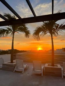 a sunset from a rooftop with palm trees and chairs at Condo Kiaraluna in Playa del Carmen