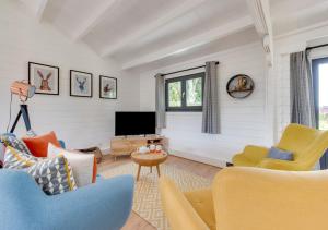 a living room with yellow and blue chairs and a television at Woodpecker Lodge in Stradbroke