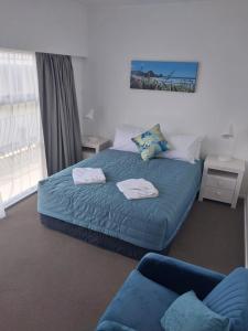 a bedroom with a bed with a blue blanket and a couch at Bayview Motel in Paihia