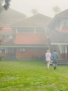 two people walking in front of a house in the rain at 3 Hills Hostel in Wayanad