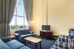 Howard Johnson Dammam Hotel في الدمام: غرفة في الفندق مع أريكة وكراسي وتلفزيون
