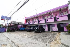 różowy budynek z samochodami zaparkowanymi przed nim w obiekcie Paus Guest House Pekanbaru w mieście Pekanbaru