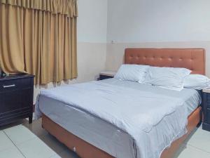 1 dormitorio con 1 cama grande con sábanas y almohadas blancas en Hotel Halmahera Palangkaraya Mitra RedDoorz en Palangkaraya