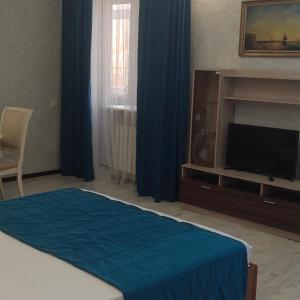 1 dormitorio con 1 cama, TV y cortinas azules en Гостиница ,,Меркурий и К,, en Astaná