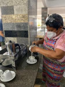 une femme portant un masque qui agite une tasse dans une cuisine dans l'établissement Hotel Art Final, à Marataizes