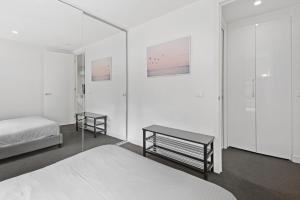 a white bedroom with two beds and a mirror at Newly Refurnished Beachside 1-Bedroom Apartment in Melbourne