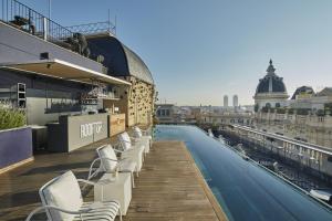 una piscina panoramica con sedie bianche in un edificio di Ohla Barcelona a Barcellona