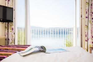 ein Bett mit einem Buch darauf mit einem Fenster in der Unterkunft Werzers Seehotel Wallerwirt in Techelsberg am Worthersee