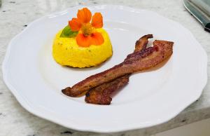 Carriage House Bed & Breakfast في وينونا: طبق من الطعام مع لحم الخنزير المقدد والأناناس الأصفر