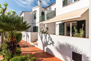 a white house with a fence and a palm tree at Apartamento Udane Menorca by Mauter Villas in Cala en Blanes