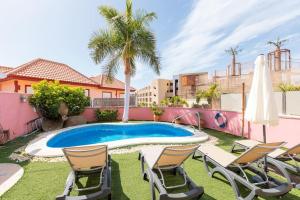 a backyard with a swimming pool and chairs and palm trees at Nice 3 Bedroom Villa in El Duque in Adeje