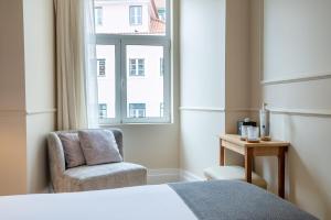 a bedroom with a bed and a chair and a window at Rossio FLH Suites in Lisbon