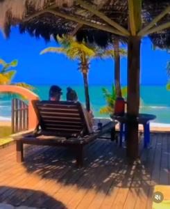 dos personas sentadas en un banco mirando el océano en Pousada Luar da Praia, en Imbassai