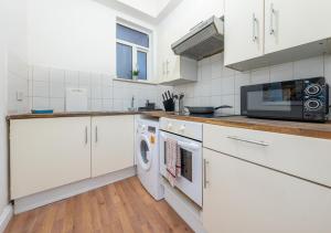 a kitchen with white cabinets and a washer and dryer at Spacious Cricklewood Apartment sleeps 4 in London