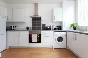 cocina con armarios blancos, lavadora y secadora en Spacious Comfortable house close to Etihad+parking en Mánchester