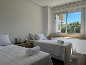 Habitación blanca con 2 camas y ventana en Apartamentos Altos da Bela Vista by Achei Gramado en Gramado
