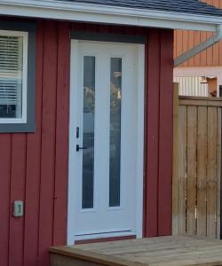 a white door on a red house with a wooden porch at Global Village Permaculture BnB in Oliver