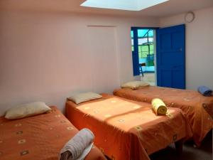 three beds in a room with orange sheets at Posada Azul Cusco in Cusco