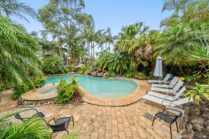 a swimming pool with chairs and a table and an umbrella at Oasis Inn Ulladulla in Ulladulla