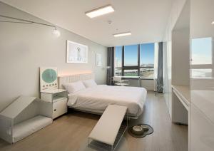 a white bedroom with a bed and a desk and window at UH FLAT THE SONGDO in Incheon
