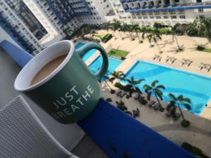 a cup of coffee on a balcony with a pool at Bliss by John at Sea Residences in Manila