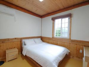 a bedroom with a white bed and a window at Geumok Log Pension in Seogwipo