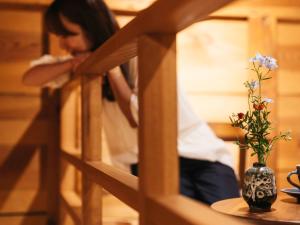 Eine Frau, die an einem Tisch mit einer Vase mit Blumen sitzt. in der Unterkunft RITA Izumo Hirata in Izumo