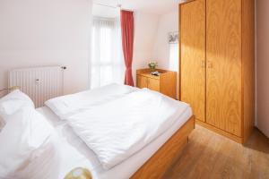 Schlafzimmer mit einem weißen Bett und einem Holzschrank in der Unterkunft Die Kogge - Wohnung 9 in Norderney