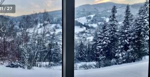 two views of a snow covered forest from a window at Apartamenty Widokowe Na Szczycie in Korbielów
